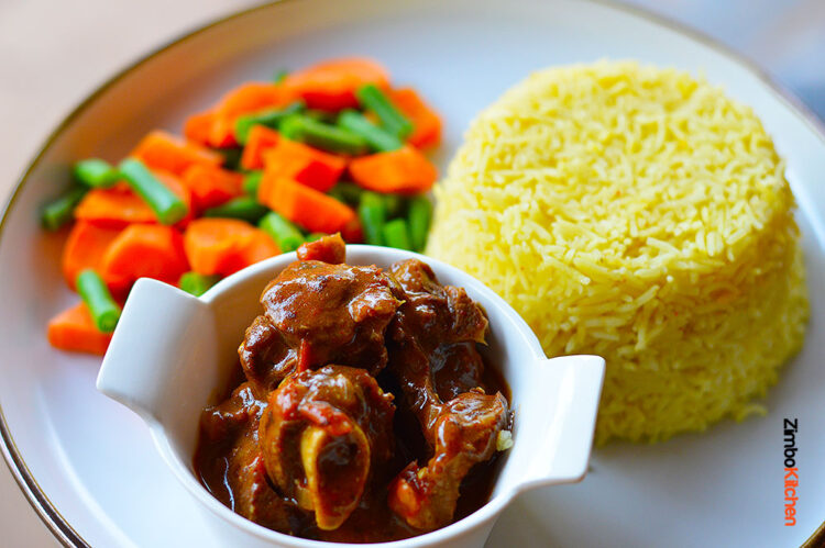 Plate with goat stew served with stemmed veggies and rice by Zimbokitchen